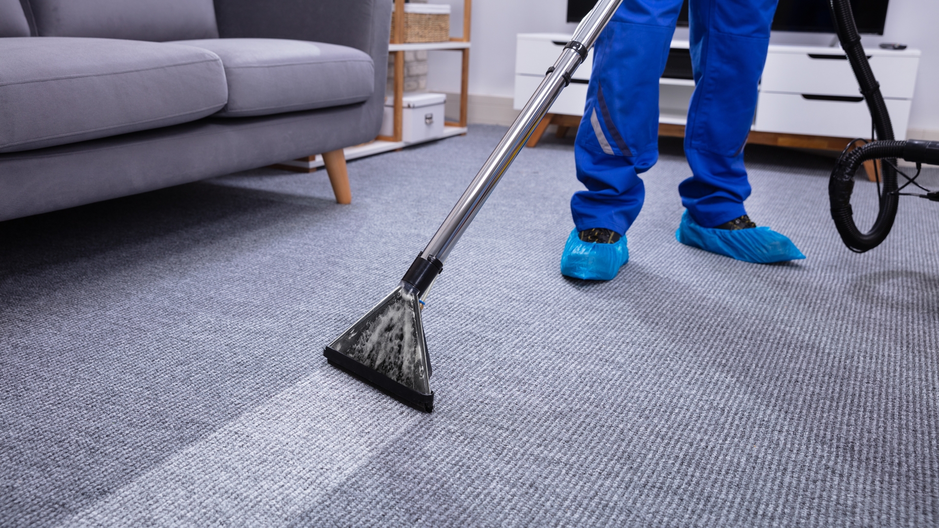 A person in blue pants and blue shoes is cleaning a carpet