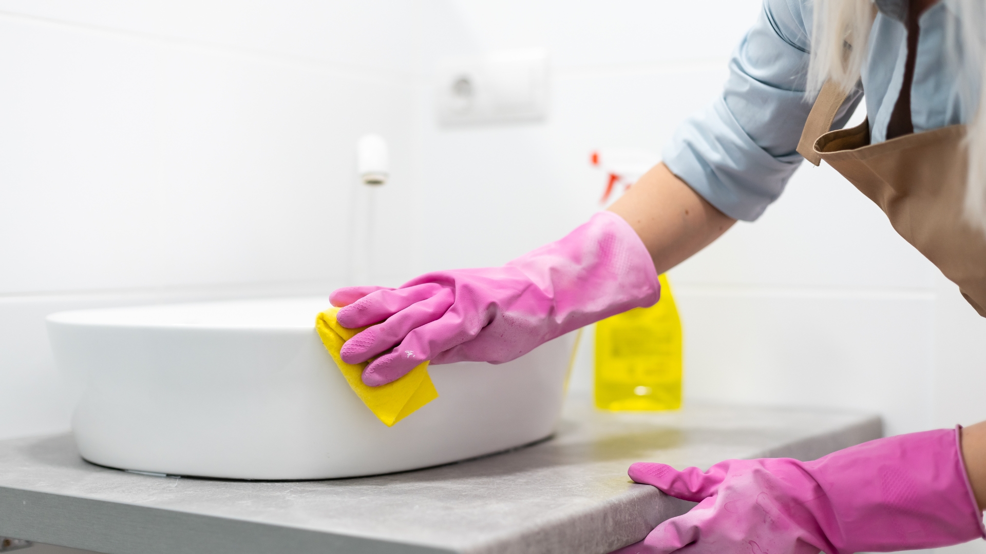 A woman in pink gloves cleaning a white sink