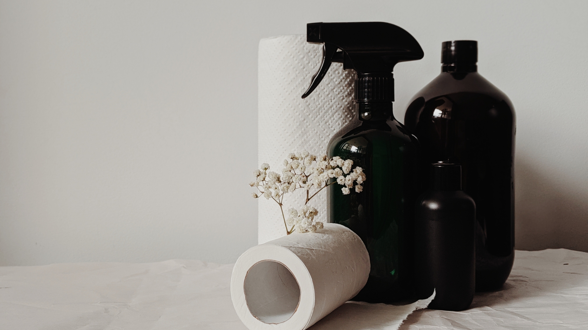 A bottle of cleaner, a spray bottle, and a roll of toilet paper on